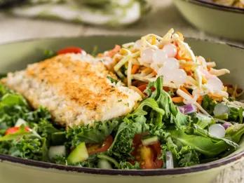 Bowl of food including some meat, salad and white circular balls.