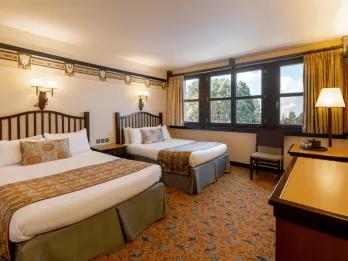 A forest/Bambi themed hotel room with two beds, a chair and a dresser