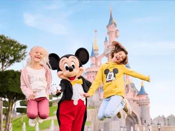 Two young girls jumping with Mickey Mouse in front of the Disneyland Paris castle