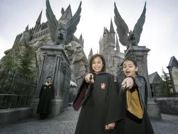 The Wizarding World of Harry Potter Two young girls wearing wizard robes and pointing magic wands at the camera while standing in front of Hogwarts Castle