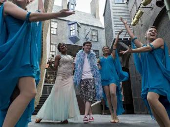 Celestina Warbeck and the Banshees Woman in a pretty, elegant floor length white and blue dress singing with a man next to her wearing a blue feather boa. Around there are three women wearing shorter blue dresses.