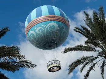 Aerophile Balloon Flight Large blue hot air balloon flying up in the sky with two palm trees either side.
