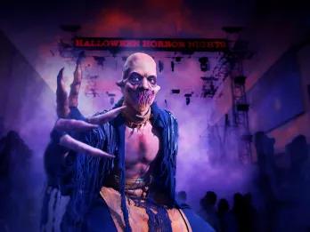 Halloween Horror Nights Bald man with scary teeth and a huge claw is staring at the camera with frightening expression. His shirt is unbuttoned and behind is purple lighting and a dark banner.