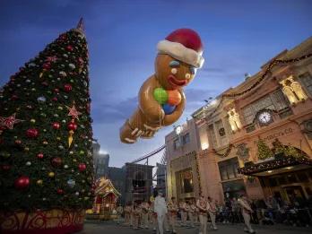 Macy's Christmas Parade Huge Christmas tree with pretty decorations on. Next to it is a giant gingerbread man in christmas Santa Claus hat floating in the air.