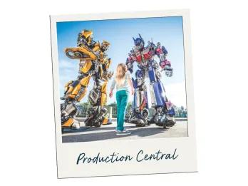 Production Central Young girl stood looking up to two giant robots, one yellow and the other blue and grey. They are Transformers. The polaroid is labelled Production Central.