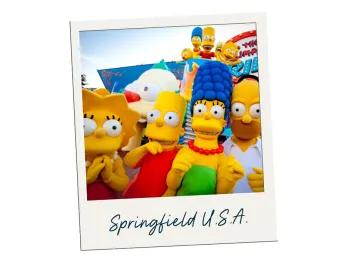 Springfield U.S.A. The four characters of the Simpsons, big yellow people cartoon characters include Homer, Marge, Bart and Lisa. They are stood in front of their ride which has giant cartoon clown face as opening. The polaroid is labelled Springfield U.S.A.