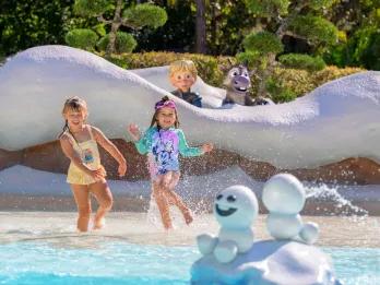 Tike's Peak Two little girls playing in a shallow pool. Behind there are snow walls and a statue of young Kristoff and Sven are poking over from Frozen. There are also statues of the small snow ball shaped snowmen in the middle splashing water.