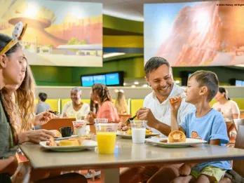 Family eating quick serve breakfast together in Disney's Art of Animation Resort. Little boy is eating bacon with his hands and the dad is smiling at him.