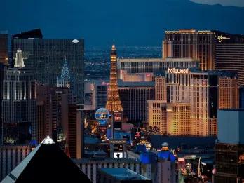 Las Vegas The strip of Las Vegas. There is a straight road with cars on it and a large pointy metal building coloured yellow with lighting, a replica of the Eiffel Tower. There is also a huge air balloon lighted in neon blue and yellow. There are many casinos and hotels as well.