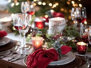Christmas dinner table set with plates, crackers and Christmas tree lights in the background.