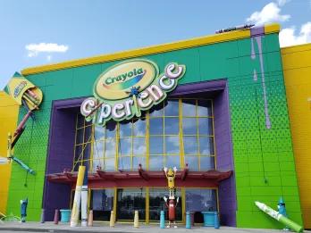Crayola Experience Large modern building coloured yellow, green and purple has big sign saying Crayola Experience on it. There are giant crayons outside with faces on them.