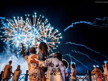 Family of three, with two parents holding up their little girl to see the fireworks in the sky better.