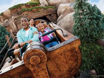 Guests sat in a mine cart coming out of a rock cave screaming and smiling.