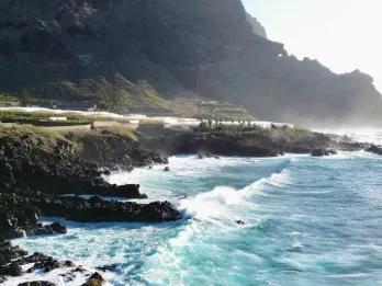 Warum Teneriffa das ganze Jahr über ein perfektes Reiseziel ist Türkisblaues Wasser wirft Wellen auf eine Küste mit Bergen im Hintergrund