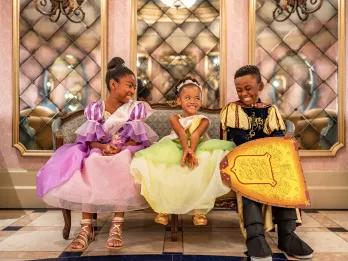 Bibbidi Bobbidi Boutique Three young children sitting on a couch dressed as princesses and a prince