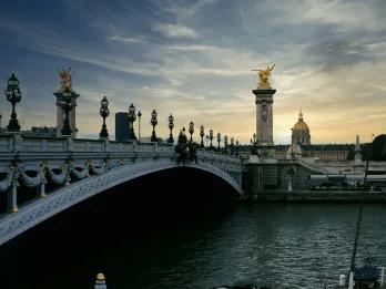 Paris at sunset A bridge over the river seine with the sunsetting in the background. there are golden statues on the bridge.