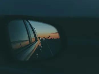 Road Trip Dark night with car mirrors and in the mirror you can see the sun setting in the background and palm trees.