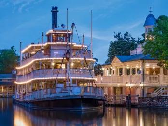 A large old-fashioned riverboat lit at dusk lit up with rows of lights