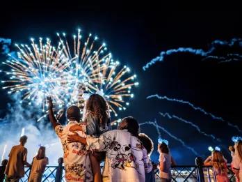 Luminous: The Symphony of Us A family standing in front of a lake watching fireworks