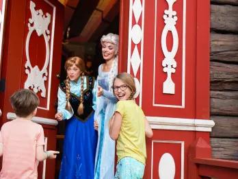 EPCOT Character Meet and Greets Anna and Elsa from Frozen opening a door to greet two young children