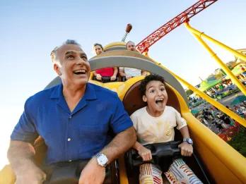 A man and young boy riding a rollercoaster designed to look like a Slinky Dog