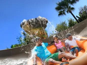 A family on a raft ride getting splashed with water from a waterfall
