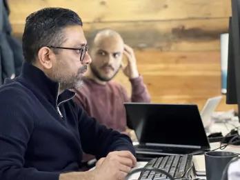 Man working on computer as another is looking over and talking to him.