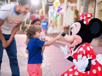 A young boy touching Minnie Mouse on the tip of her nose