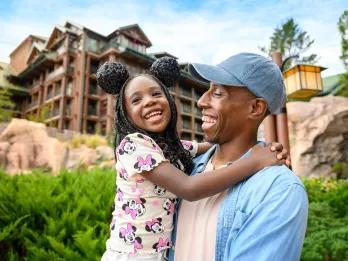 A man holding a young girl in front of a log cabin-style building
