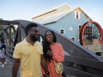 A man and woman walking arm in arm next to a building designed to look like an old mill