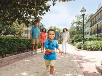 A young boy running ahead of his family as they walk past New Orleans-style buildings