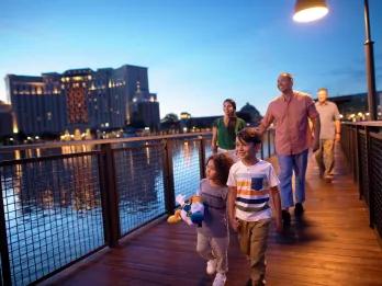 A family walking along a boardwalk at dusk with a tower building behind them