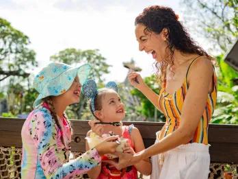 Disney Typhoon Lagoon Water Park Mum with her two kids sharing a tub of ice cream in front of the statue of a shipwreck on a tall mountain.
