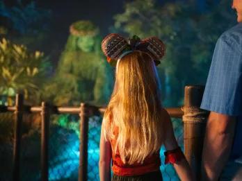 Huge statue made of grass and plants of Tefiti from Moana. A girl is stood looking at it dressed as Moana with matching Mickey Ears and holding her dads hand.