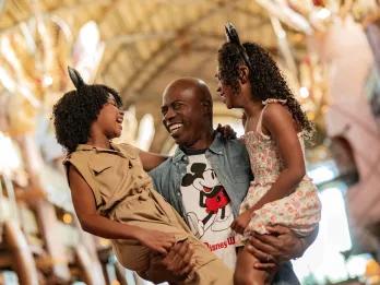 Guests at Disney's Animal Kingdom Lodge Man wearing a Mickey Mouse shirt holding two girls who are wearing safari style outfits and Mickey Mouse ears.