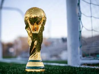 FIFA 2026 World Cup A gold trophy with a globe at the top and things wrapping around it sat in front of a white football goal.
