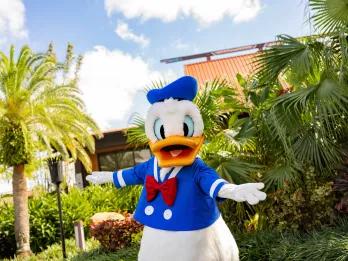 Disney's Polynesian Village Resort Donald Duck dressed in his blue sailor style suit with his arms extended open in front of a Hawaiian themed hotel.