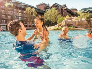 A family playing in a swimming pool in front of a cabin-style building
