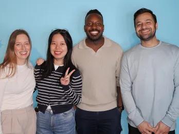 Two men and two women posing in front of a blue screen, all smiling and happy.