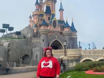Caron Smiling female in red top and red Disney ears stood in front of Disney castle