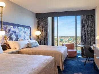Universal Helios Grand Hotel, a Loews Hotel Two double beds with a floral headboard and dark blue carpets. The curtains are drawn and in the background you can see Universal Epic Universe.