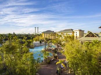 Loews Royal Pacific Resort Large yellow resort with small river in front where the boats take guests to the park. In the background is a double drop tower and other rides in the parks.