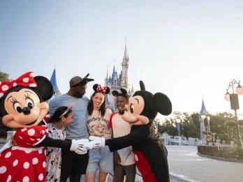 A family hugging Mickey and Minnie Mouse in front of Cinderella Castle