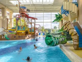 Large pool with green dragon themed water slide heading into it. There is also a climbing frame water park area.