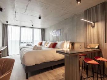 Two double beds in a large room and a counter with two orange stools.