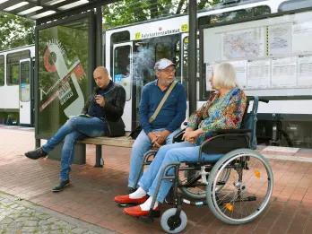Woman in wheelchair talking to old man at the bus stop.