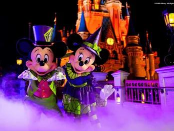 Mickey and Minnie Mouse in Halloween costumes standing in front of Cinderella Castle