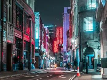 Dark street with city signs and lights lighting up the road. There is a large sign saying SOHO hanging.