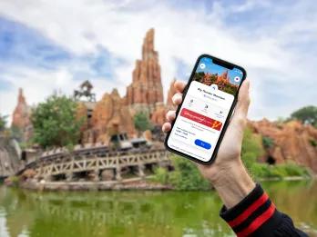 Disney Premier Access Person holding up phone with fast pass system on it in front of Big Thunder Mountain.