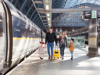 Eurostar Family of five walking along a train platform hand in hand with a bright yellow suitcase ready to board the Eurostar parked.